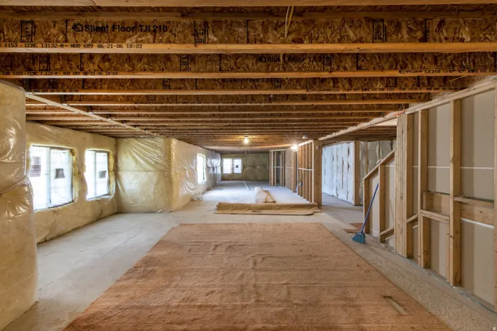 Unfinished basement featuring exposed wood joists and subflooring, framed wall partitions, and insulation