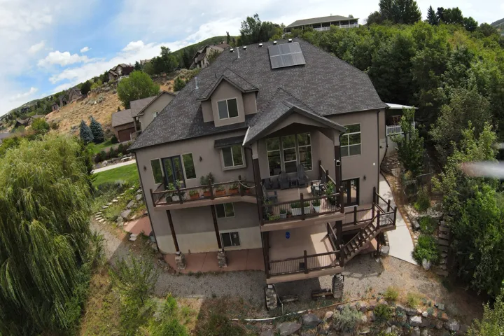 Multi-level deck and balcony system, solar panel array, dormer window, extensive exterior fenestration, and natural rock landscaping