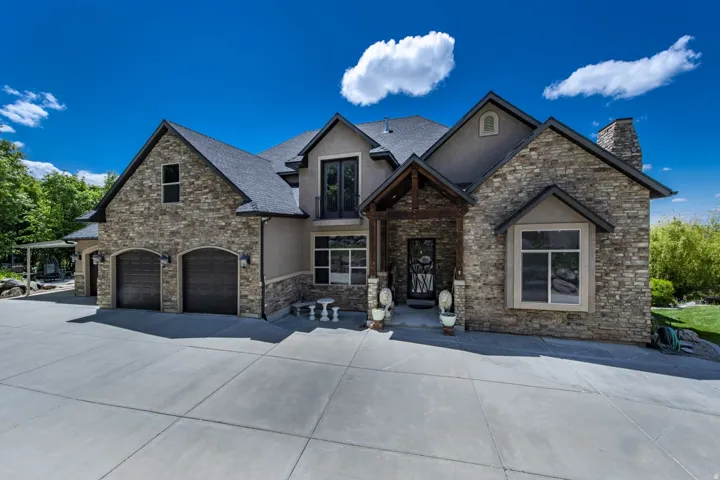 Stone and stucco exterior, multiple gables, covered entry, attached two-car garage with arched doors, concrete driveway