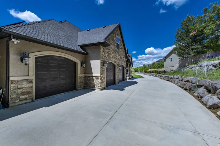 Multi-car garage with arched doors, stone facade, stucco exterior, and concrete driveway