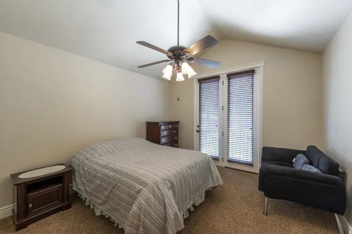 Vaulted ceiling with a ceiling fan, dual glass-paned doors with blinds, and neutral carpet flooring