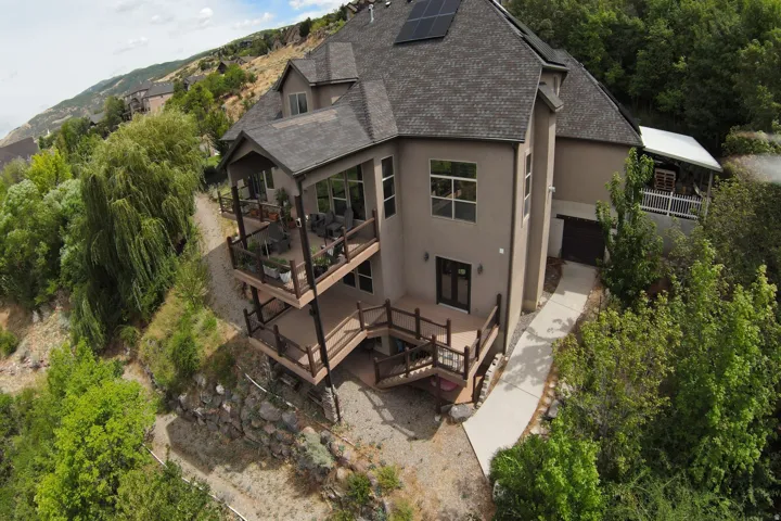 Multi-level exterior decks with dark wood railings, mature landscaping, concrete walkway, and solar panels