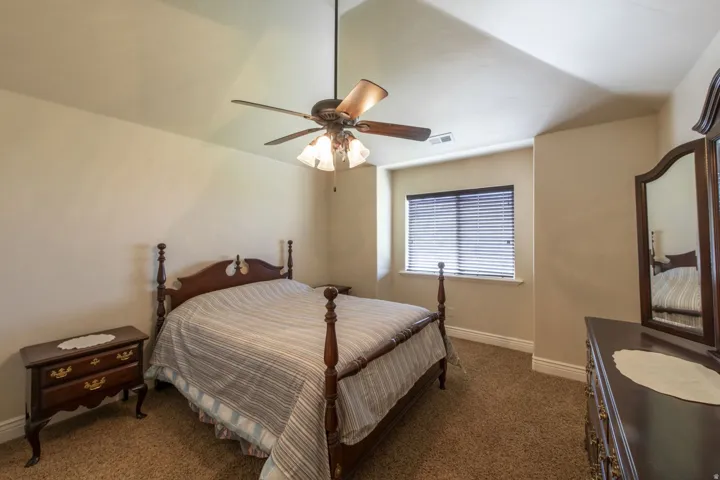Vaulted ceiling, ceiling fan with light fixture, window with blinds, and carpeted flooring