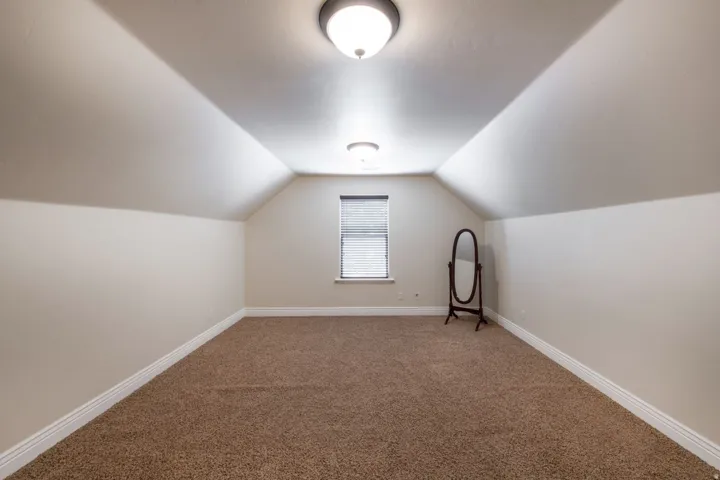 Window with blinds, vaulted ceiling, flush mount lighting, and neutral tone carpeting