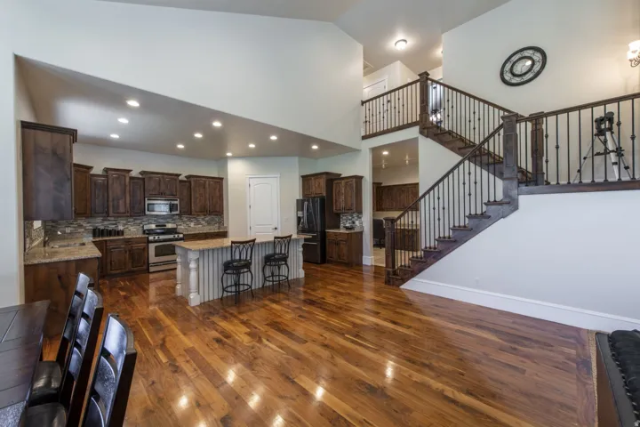 Hardwood flooring throughout, a kitchen featuring dark wood cabinetry, stainless steel appliances, a tiled backsplash, and a central island with seating, complemented by a prominent staircase with dark wood and wrought iron railings