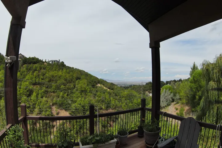 Expansive outdoor deck with dark wood-finish flooring and black metal railings, set against a backdrop of lush green hills and distant scenery