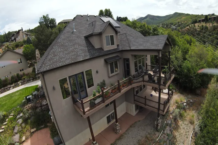 Multi-level exterior decks, shingle roof, solar panels, stucco siding, and surrounding natural landscape