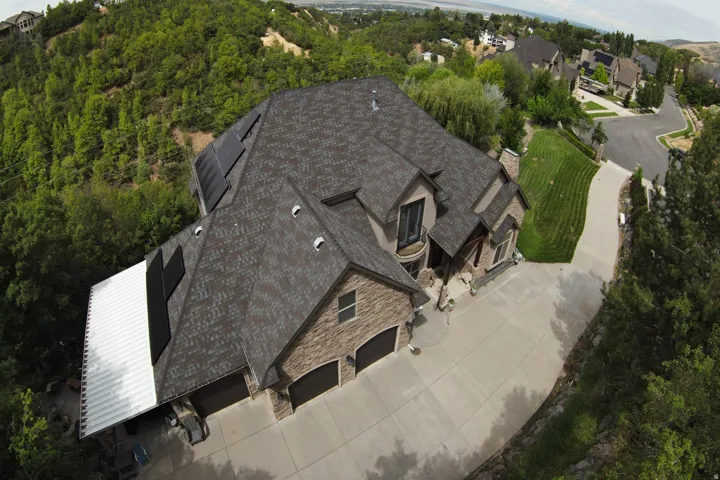 Expansive concrete driveway, attached three-car garage, stone and stucco exterior, asphalt shingle roof, and integrated solar panels