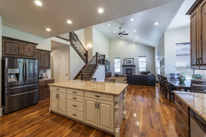 Open-concept living space with wood-finish flooring, a central kitchen island with granite countertop, dark wood cabinetry, and a vaulted ceiling