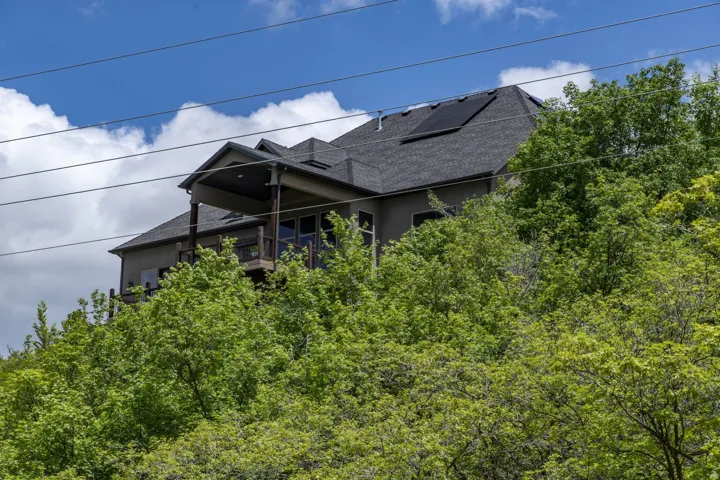 Multi-level residential structure with a covered balcony, dark shingle roof, and integrated solar panels