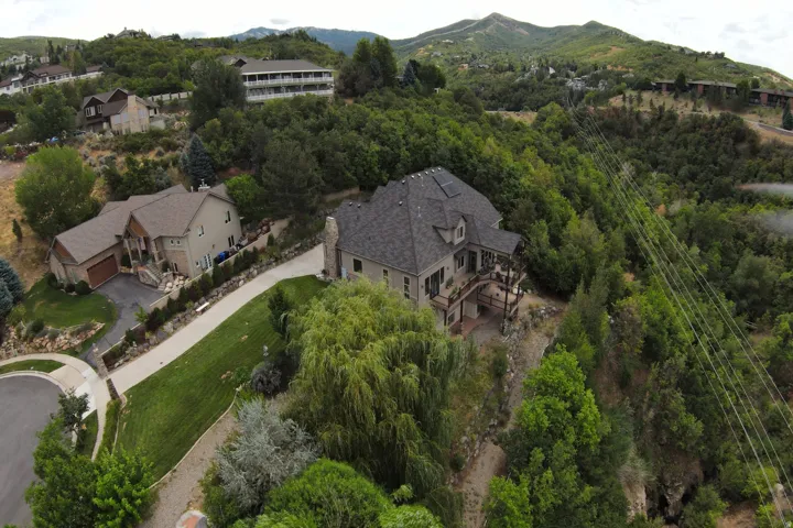 Expansive terraced property with a multi-level deck, surrounding mature trees, and mountainous backdrop