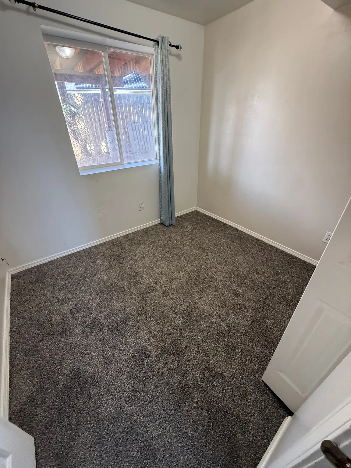 Neutral wall paint with textured finish, dark gray carpeting, and a white-framed window