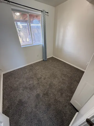 Neutral wall paint with textured finish, dark gray carpeting, and a white-framed window