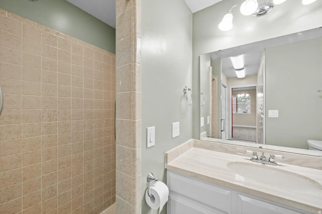 Tiled shower enclosure, vanity with integrated sink, stone-finish countertop, wall-mounted mirror, and overhead vanity lighting
