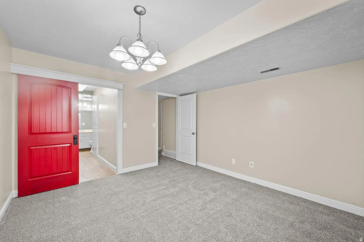 Carpeted room featuring a red barn door, white paneled interior door, and a five-light chandelier