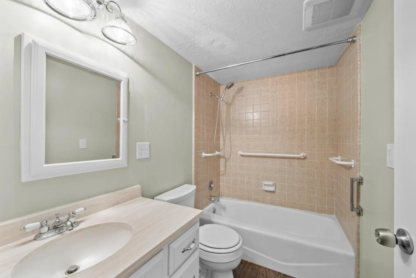 Bathroom featuring a white vanity with integrated sink, chrome faucet, wall-mounted medicine cabinet, and a tiled shower with grab bars