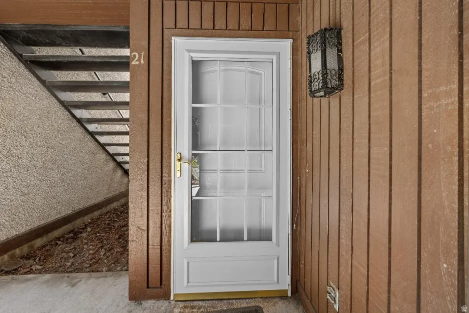 White entry door with grid-pane glass and brass hardware, complemented by a decorative wall-mounted sconce