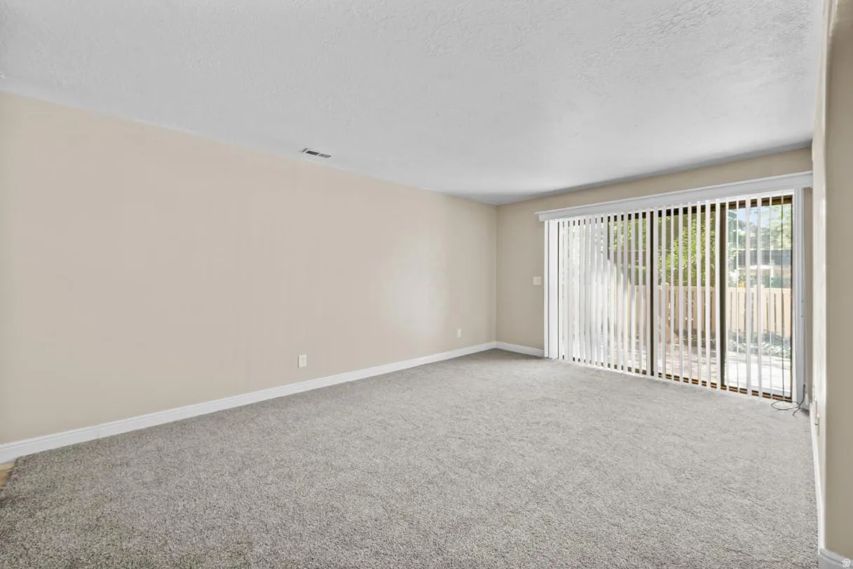 Neutral wall paint, gray carpet flooring, and a sliding glass door with vertical blinds