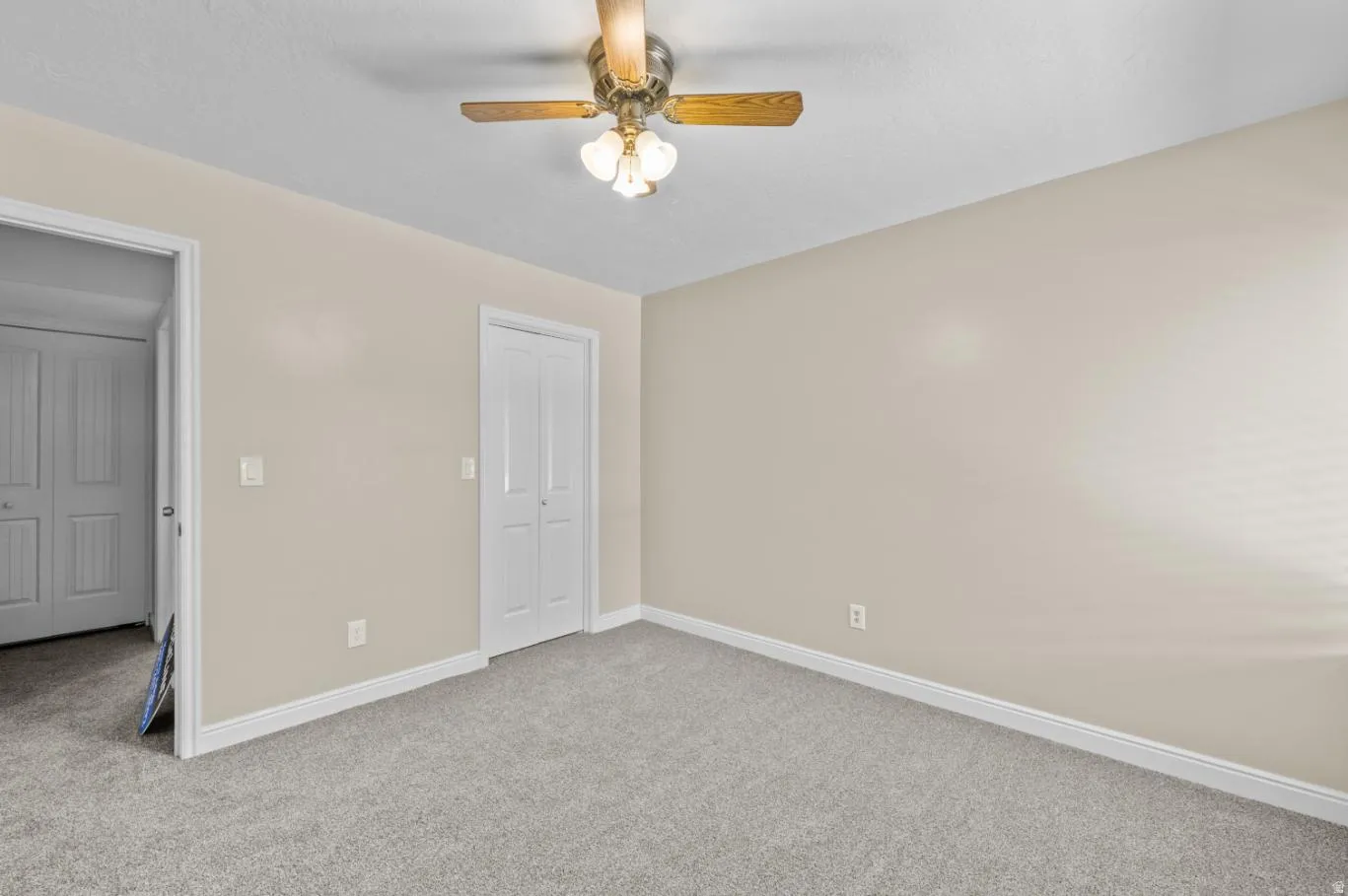 Neutral wall color, carpeted flooring, white trim, white bi-fold doors, and a ceiling fan with integrated lighting