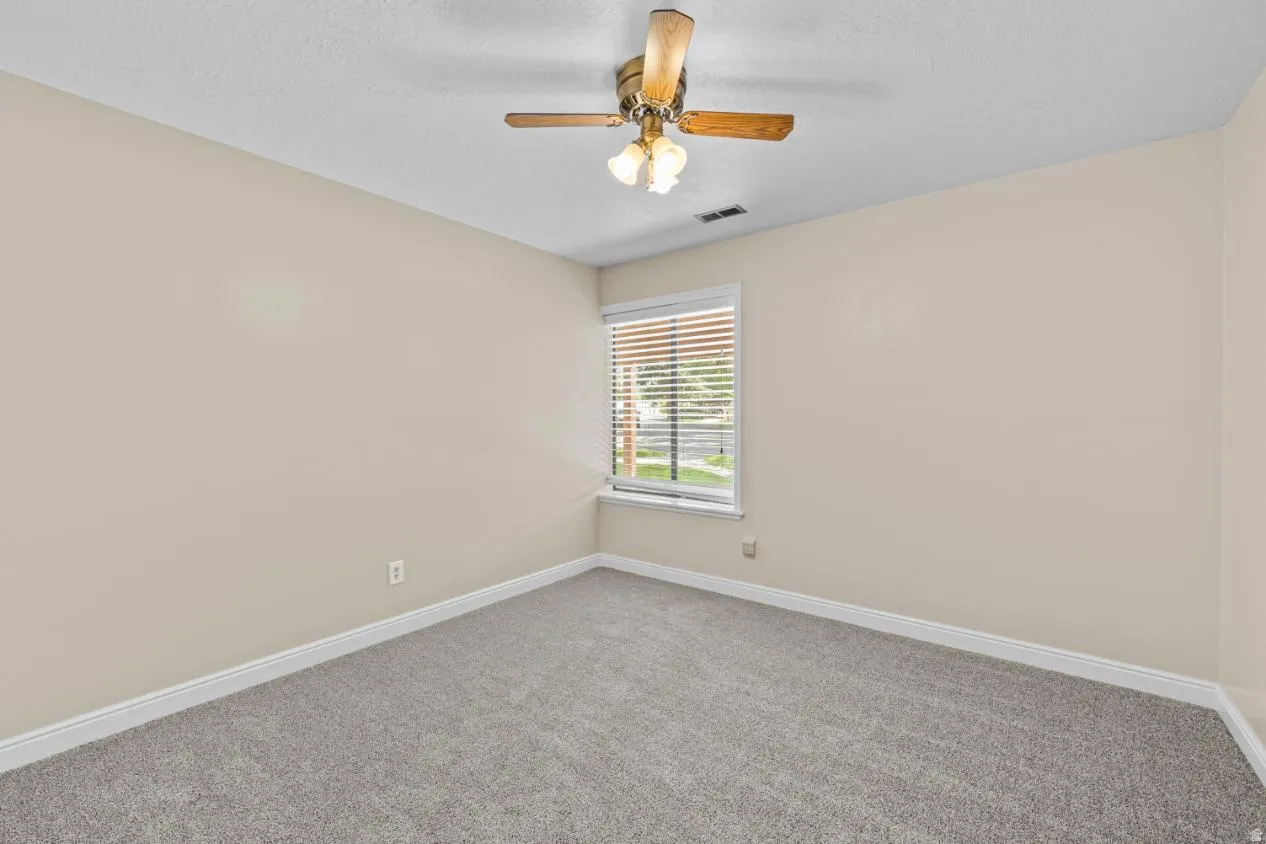 Carpeted flooring, neutral wall tones, single window with blinds, and a ceiling fan with integrated lighting