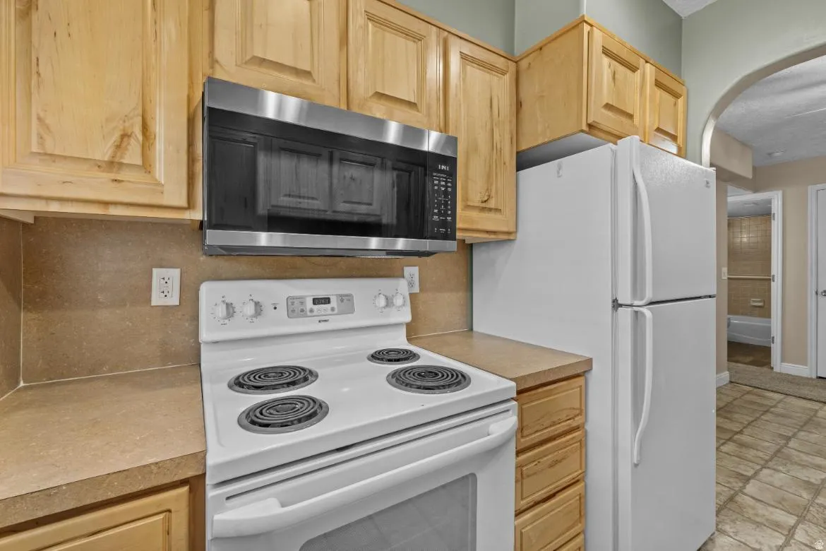 Wood-finish cabinetry, built-in stainless steel microwave, white electric range, and white refrigerator