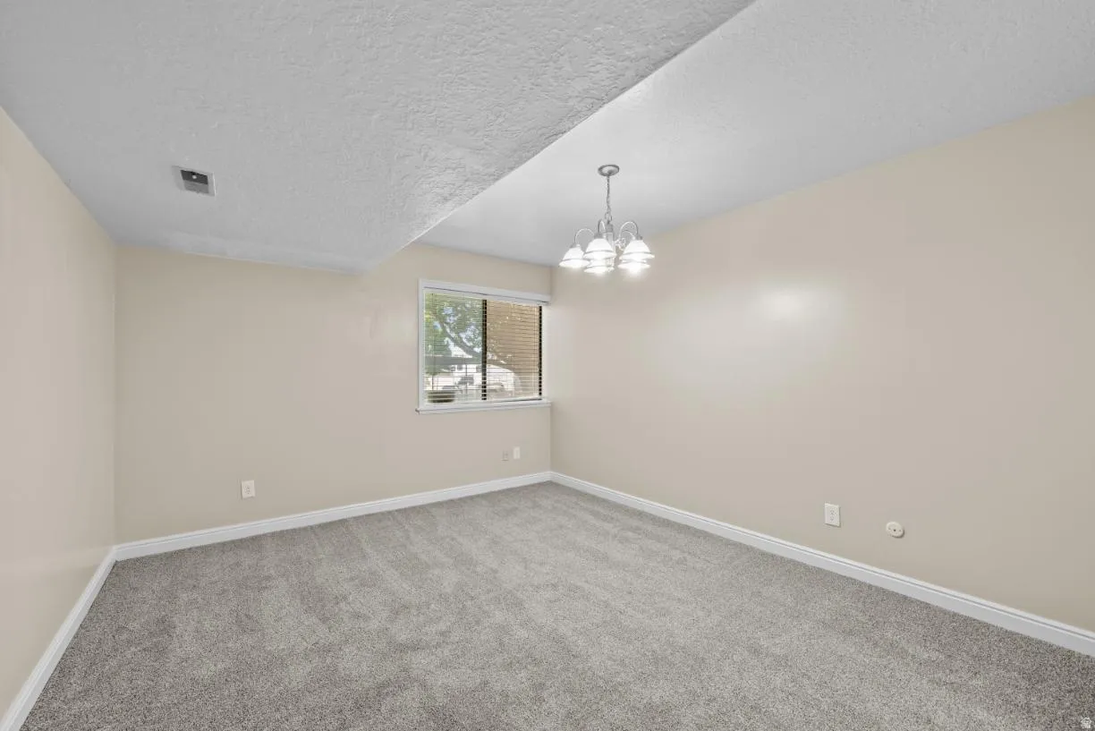 Neutral wall paint, gray carpet flooring, white trim, window with natural light, and a polished chrome chandelier