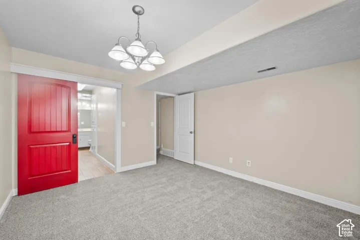 Carpeted room featuring a red barn door, white paneled interior door, and a five-light chandelier