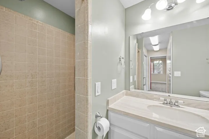 Tiled shower enclosure, vanity with integrated sink, stone-finish countertop, wall-mounted mirror, and overhead vanity lighting