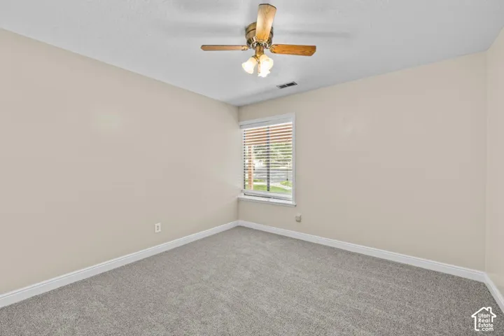 Carpeted flooring, neutral wall tones, single window with blinds, and a ceiling fan with integrated lighting