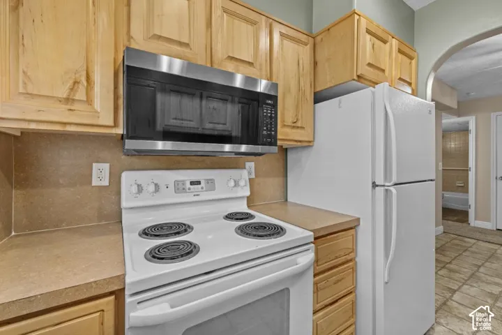 Wood-finish cabinetry, built-in stainless steel microwave, white electric range, and white refrigerator