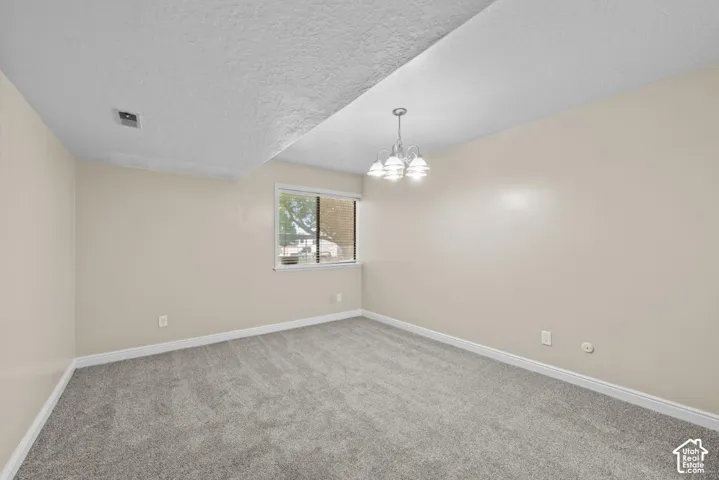 Neutral wall paint, gray carpet flooring, white trim, window with natural light, and a polished chrome chandelier