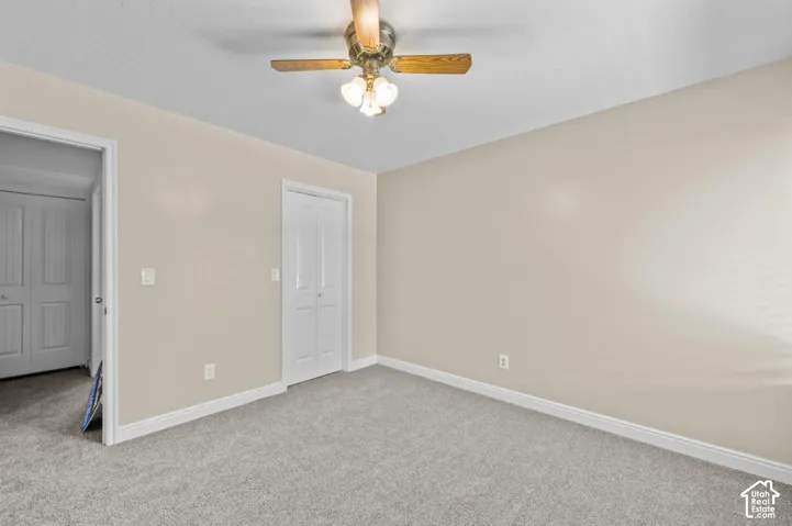Neutral wall color, carpeted flooring, white trim, white bi-fold doors, and a ceiling fan with integrated lighting