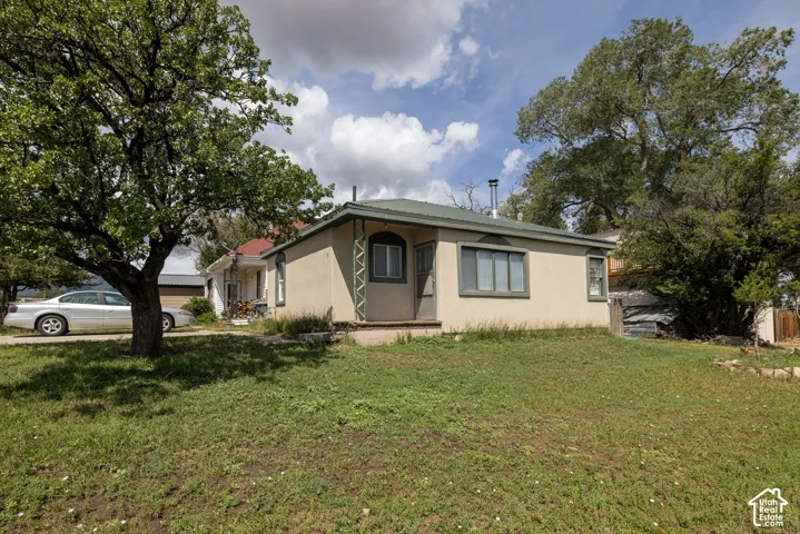 Stucco exterior, metal roof, front yard, mature trees, and a gravel driveway