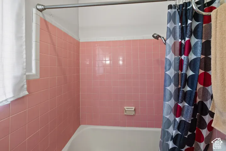 Bathtub with pink tiled shower surround and white window trim