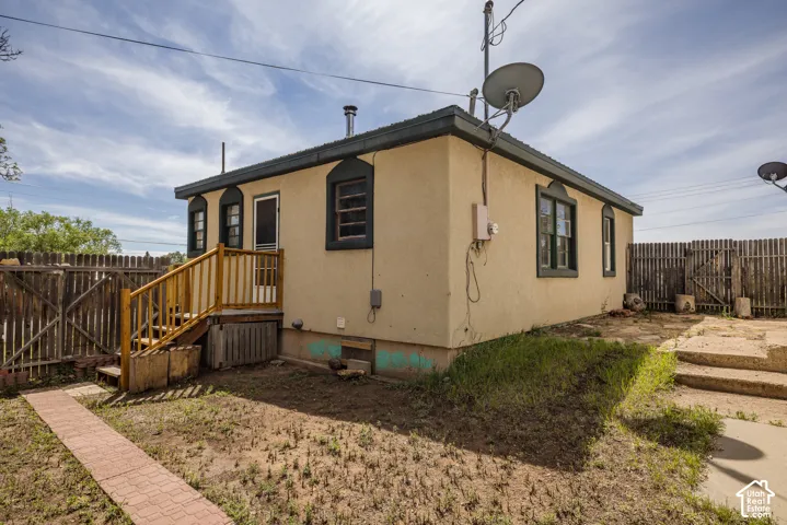 Stucco exterior with multiple windows, wood deck with stairs, brick paver pathway, and wood fencing