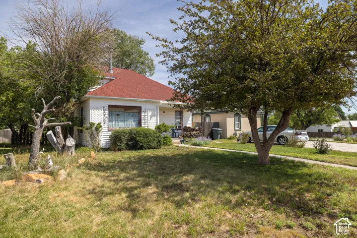 Charming cottage with a red hip roof and white exterior siding, set on a spacious lawn dotted with mature shade trees