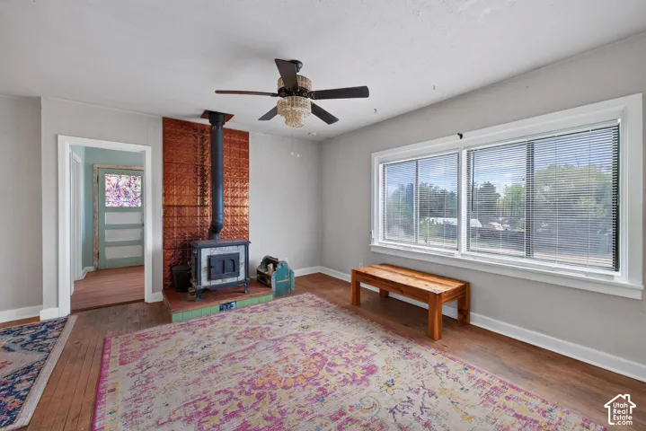 Wood-finish flooring, wood-burning stove with copper-toned wall surround, ceiling fan with integrated lighting, and multiple windows