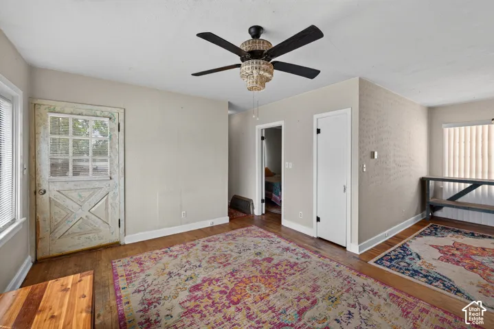 Wood-finish flooring with a decorative ceiling fan, a paneled door with glass inserts, and a window with blinds