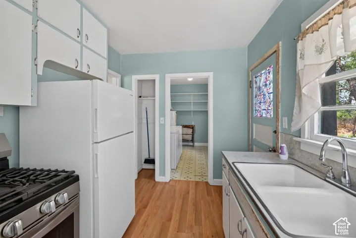White cabinetry with hardware, wood-finish flooring, stainless steel gas range, double basin sink with chrome faucet, and additional storage shelving