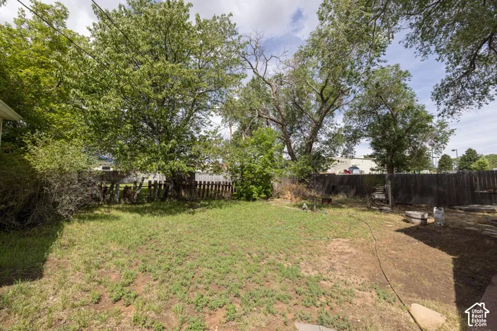 Spacious backyard with mature shade trees and established lawn, fenced perimeter, and outbuilding structures visible on the property
