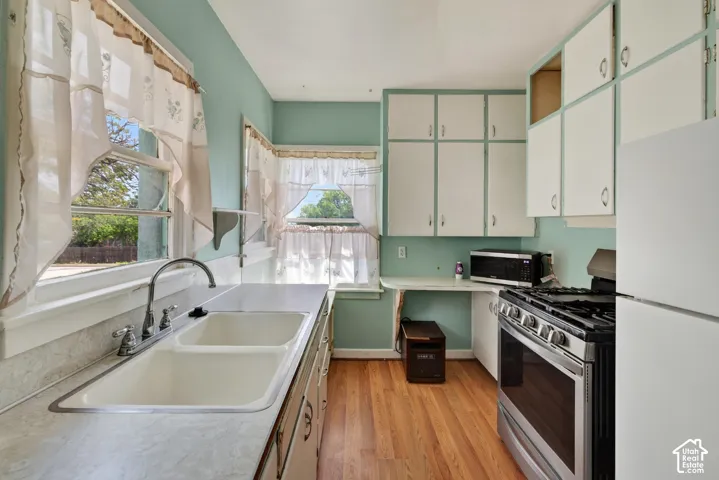 Kitchen featuring wood-finish flooring, white cabinetry, a dual-basin sink with a chrome faucet, and a stainless steel oven