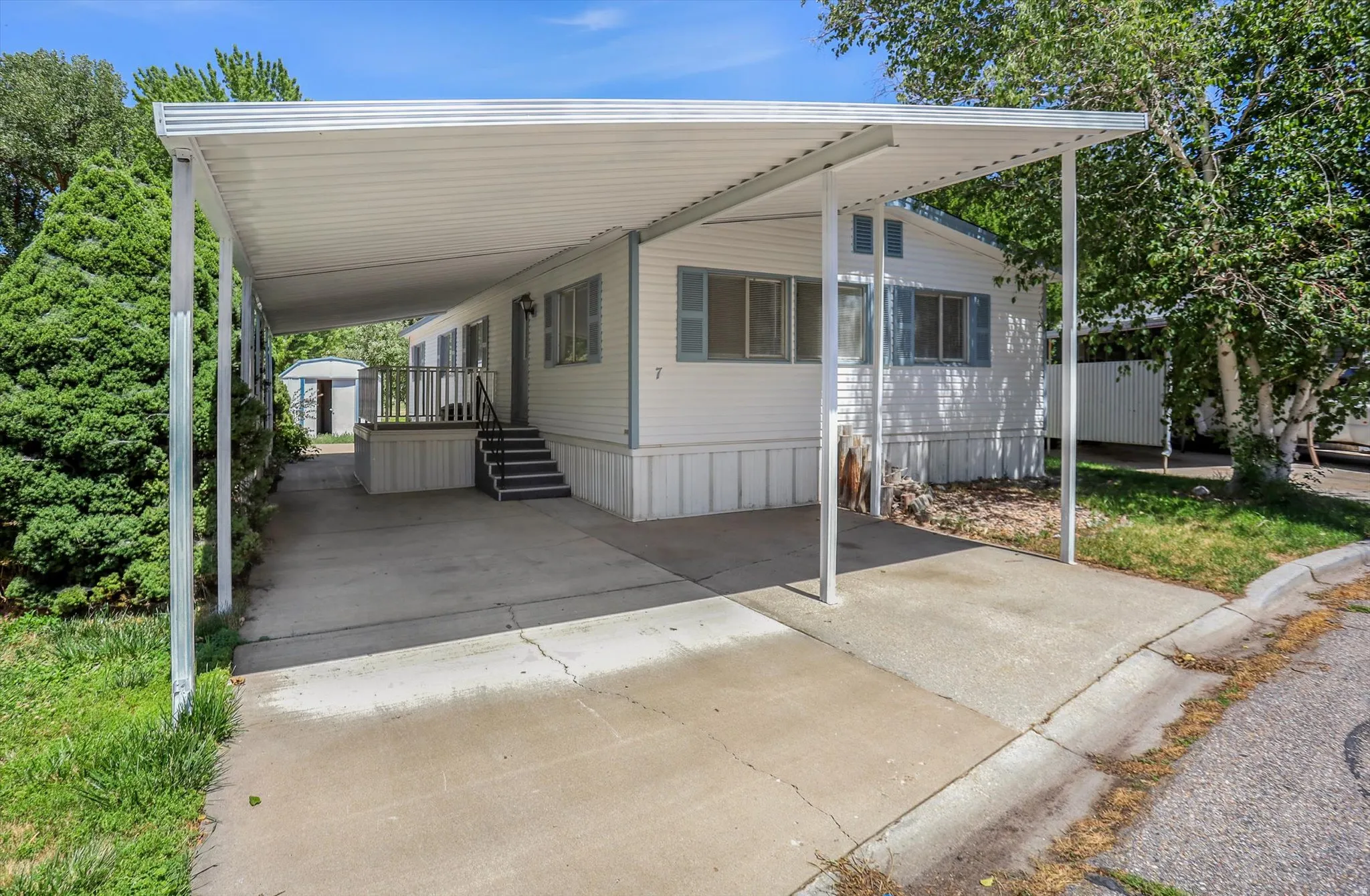 White siding exterior with a covered carport, concrete driveway, and front entry stairs