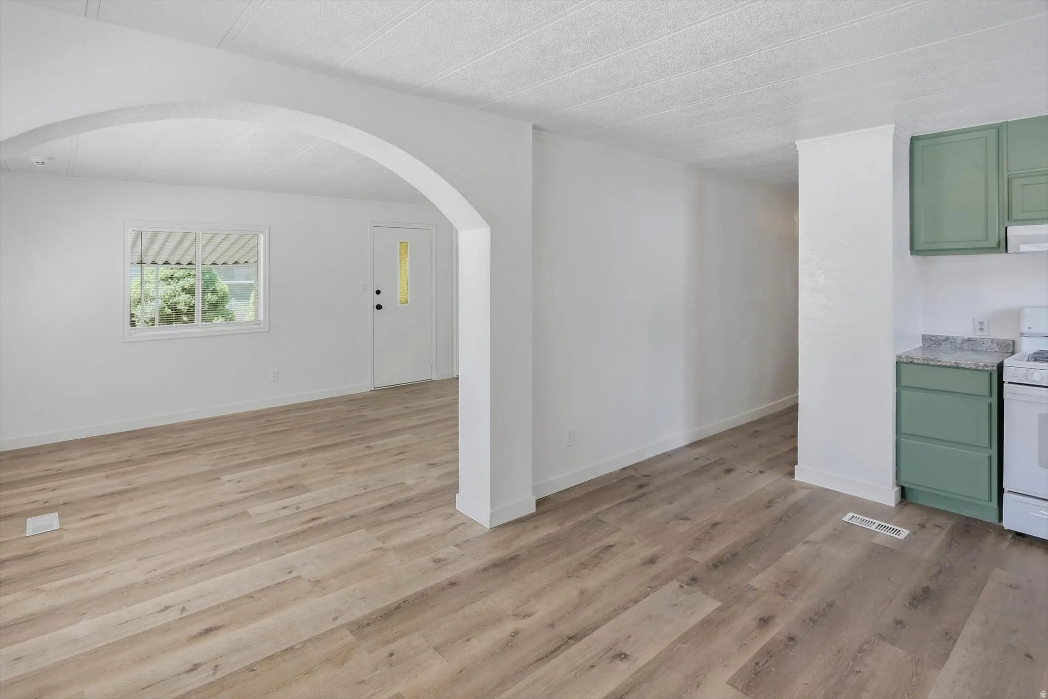 Wood-finish flooring throughout, archway detailing, white interior walls, white paneled entry door with window insert, and green cabinetry with light-colored countertops