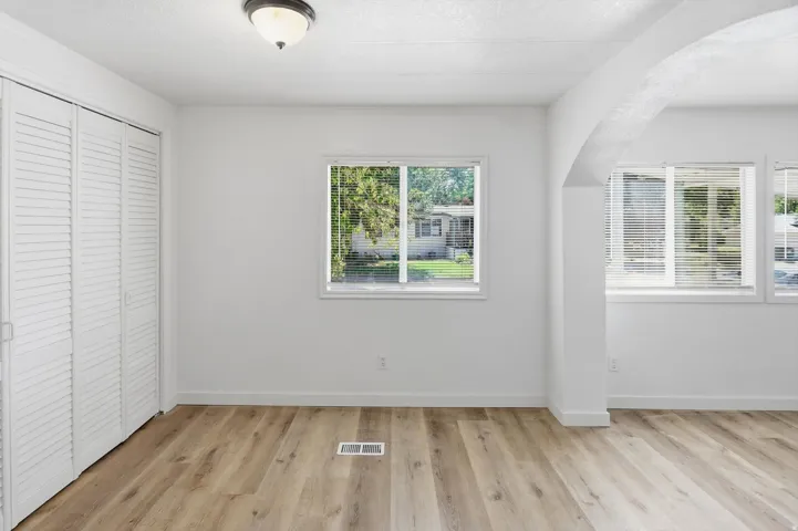 Light wood-finish flooring, white louvered closet doors, multiple windows with blinds, and a structural archway