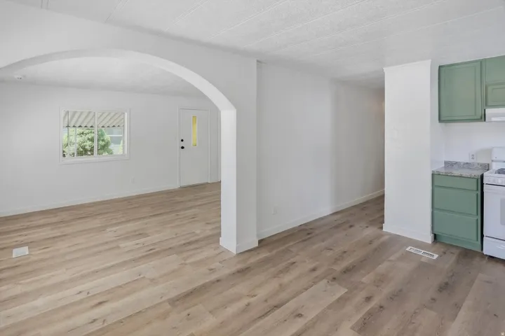 Wood-finish flooring throughout, archway detailing, white interior walls, white paneled entry door with window insert, and green cabinetry with light-colored countertops