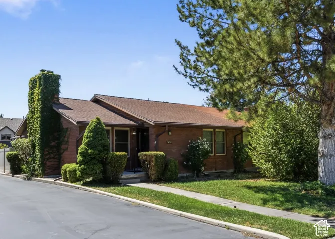 Single-story brick exterior featuring an exterior chimney, asphalt shingle roof, and mature landscaping