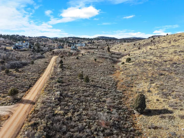 Expansive undeveloped land with a dirt road, varied terrain, and distant residential structures