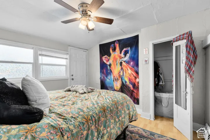 Wood-finish flooring, ceiling fan with integrated lighting, multiple windows with blinds, a white paneled door, and a white French door