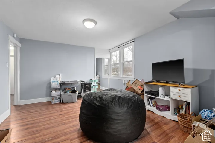 Spacious recreation room featuring warm wood-finish flooring, soft blue-gray walls, and ample natural light from large windows