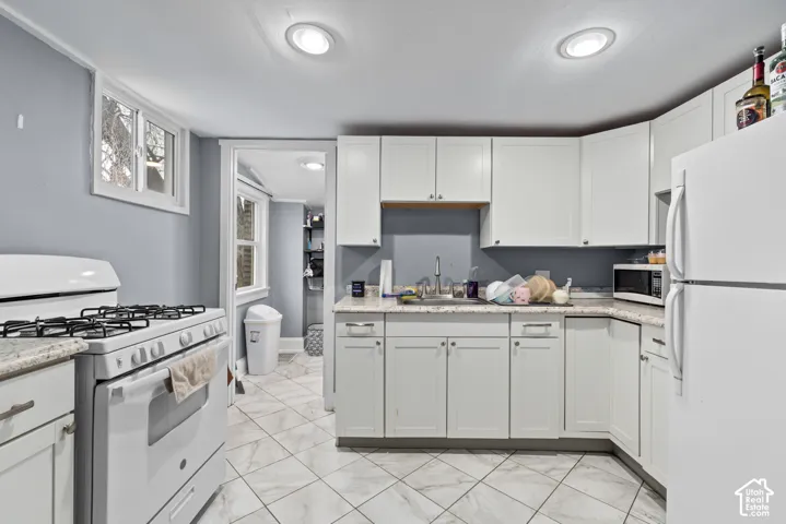 White cabinetry with silver hardware, light-toned countertops, white tile flooring, recessed ceiling lighting, and a white gas range